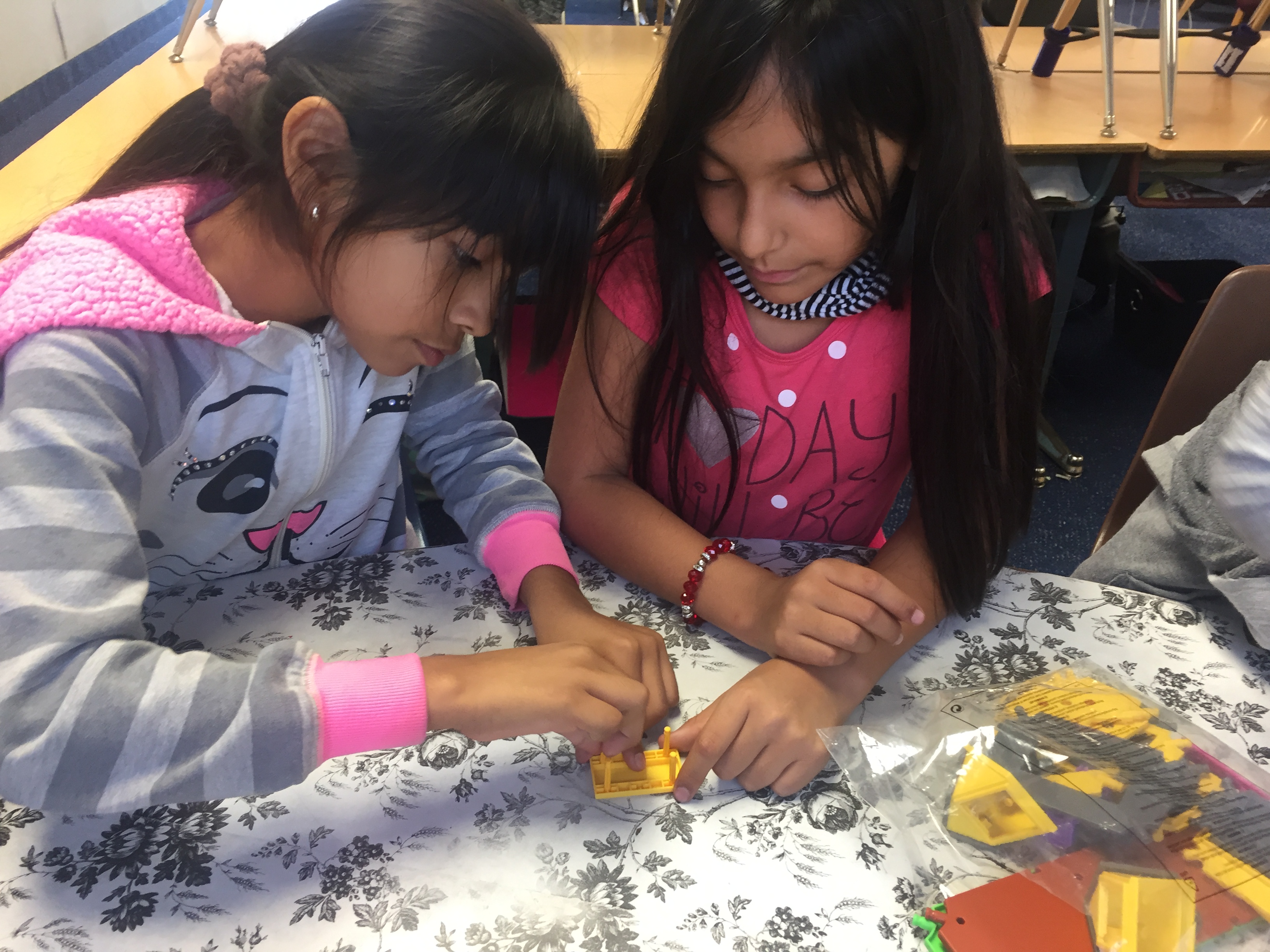A pair of students work on constructing a model house and analyze each step as they go.