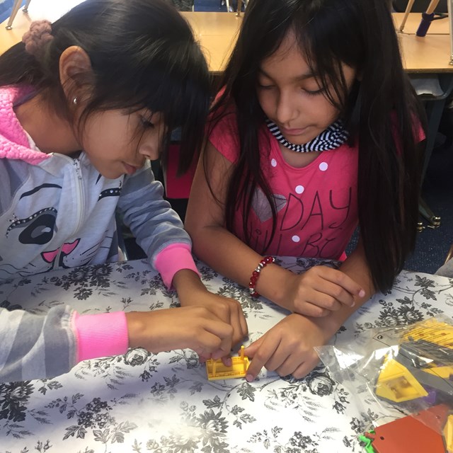 A pair of students work on constructing a model house and analyze each step as they go.